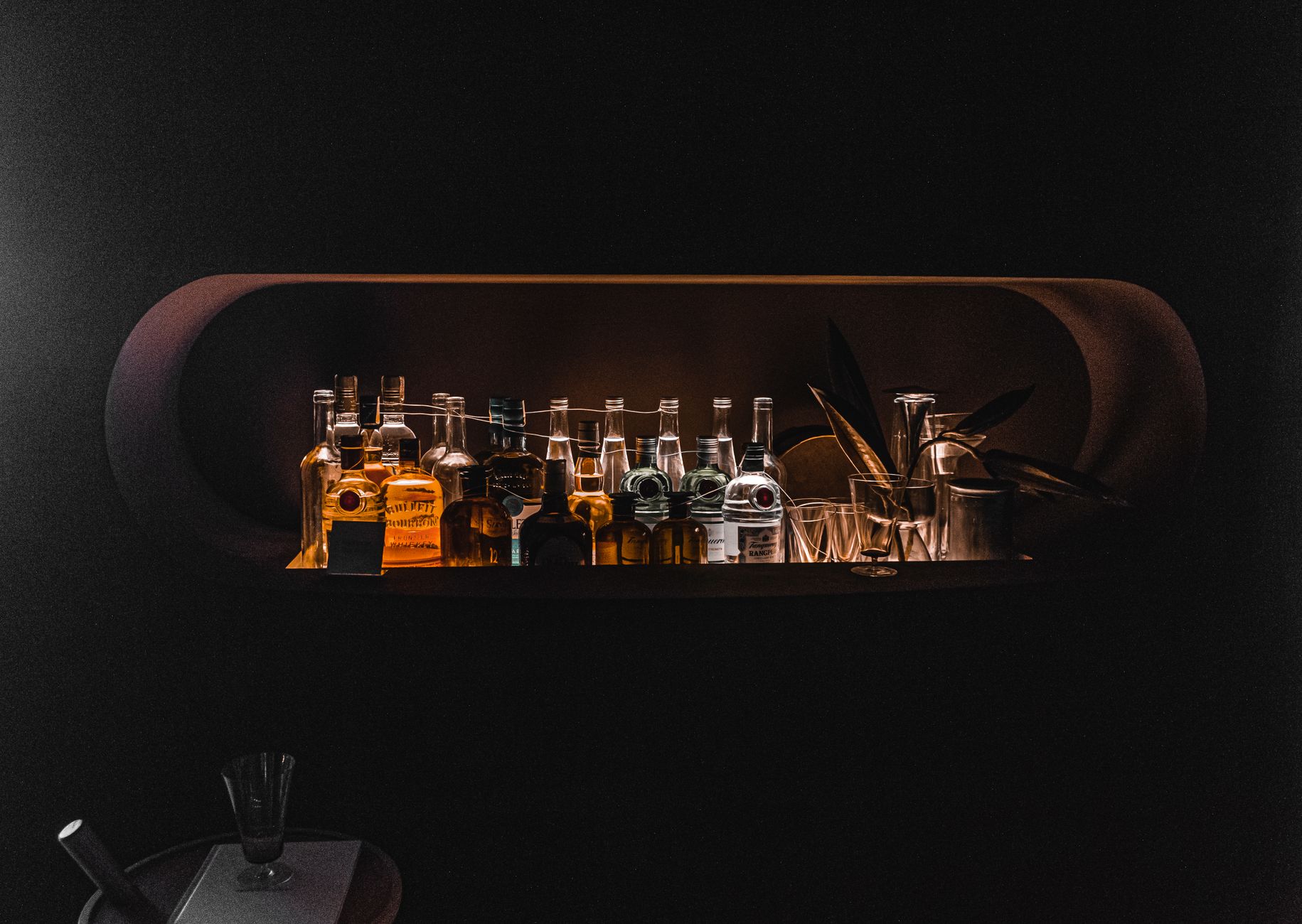 Glas og flasker i roligt lys bag en bar